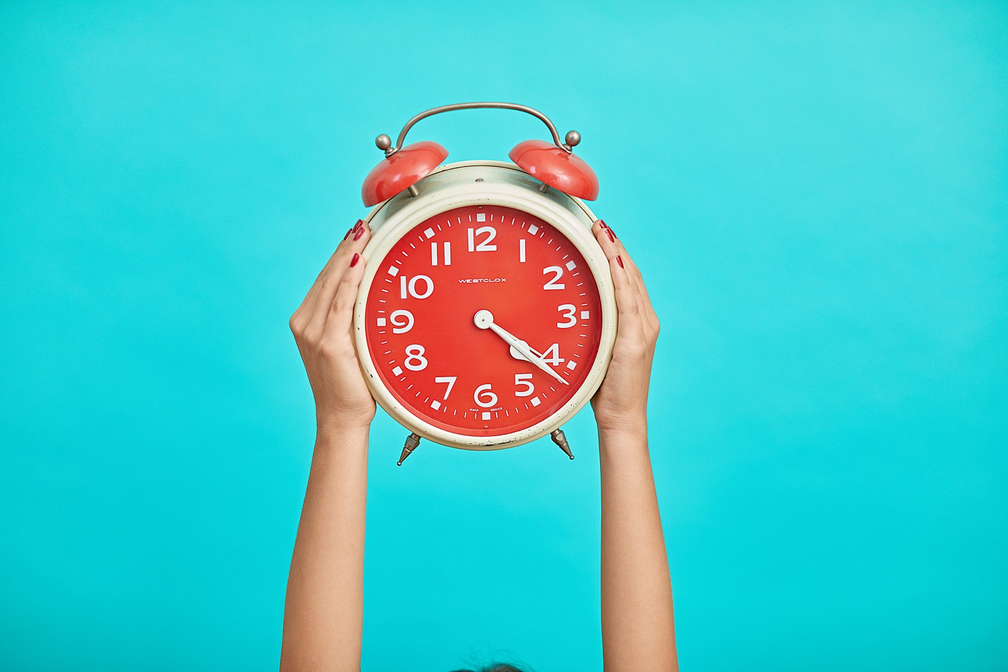 Person holding red clock on a teal background