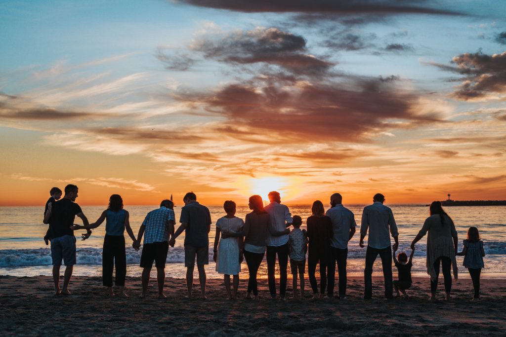 a large group of people standing on a beach at sunset, their diversity apparent