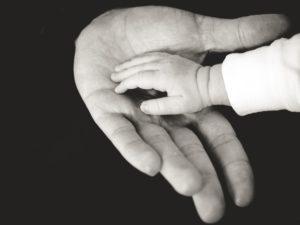 a baby's hand on top of an adult hand with a black background