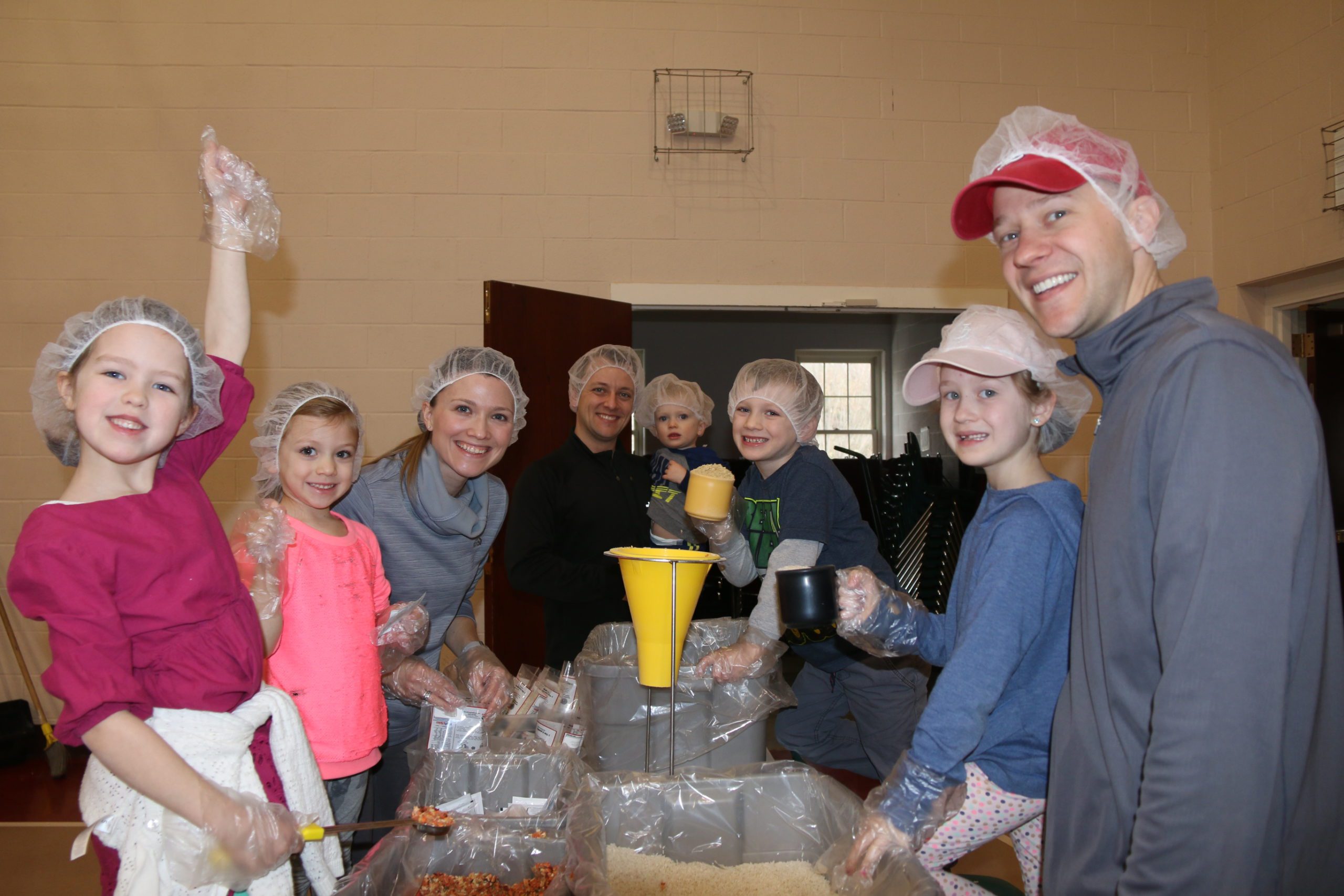 volunteer kids and adults wearing hair nets and packaging food for those in need