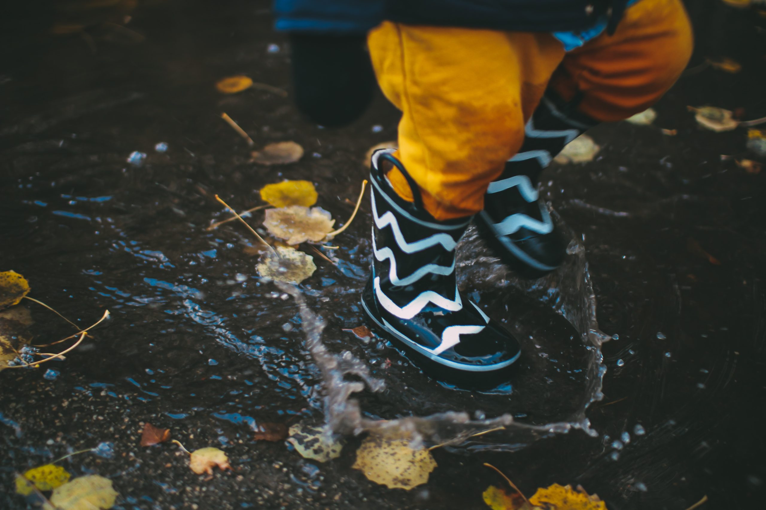 child splashing in a puddle with boots on