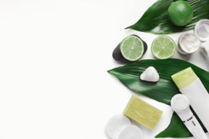 Going green with natural skincare products on big green leaves at white table, top view