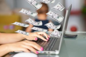Work from home mom on her laptop with dollars flying around as her child plays in the background