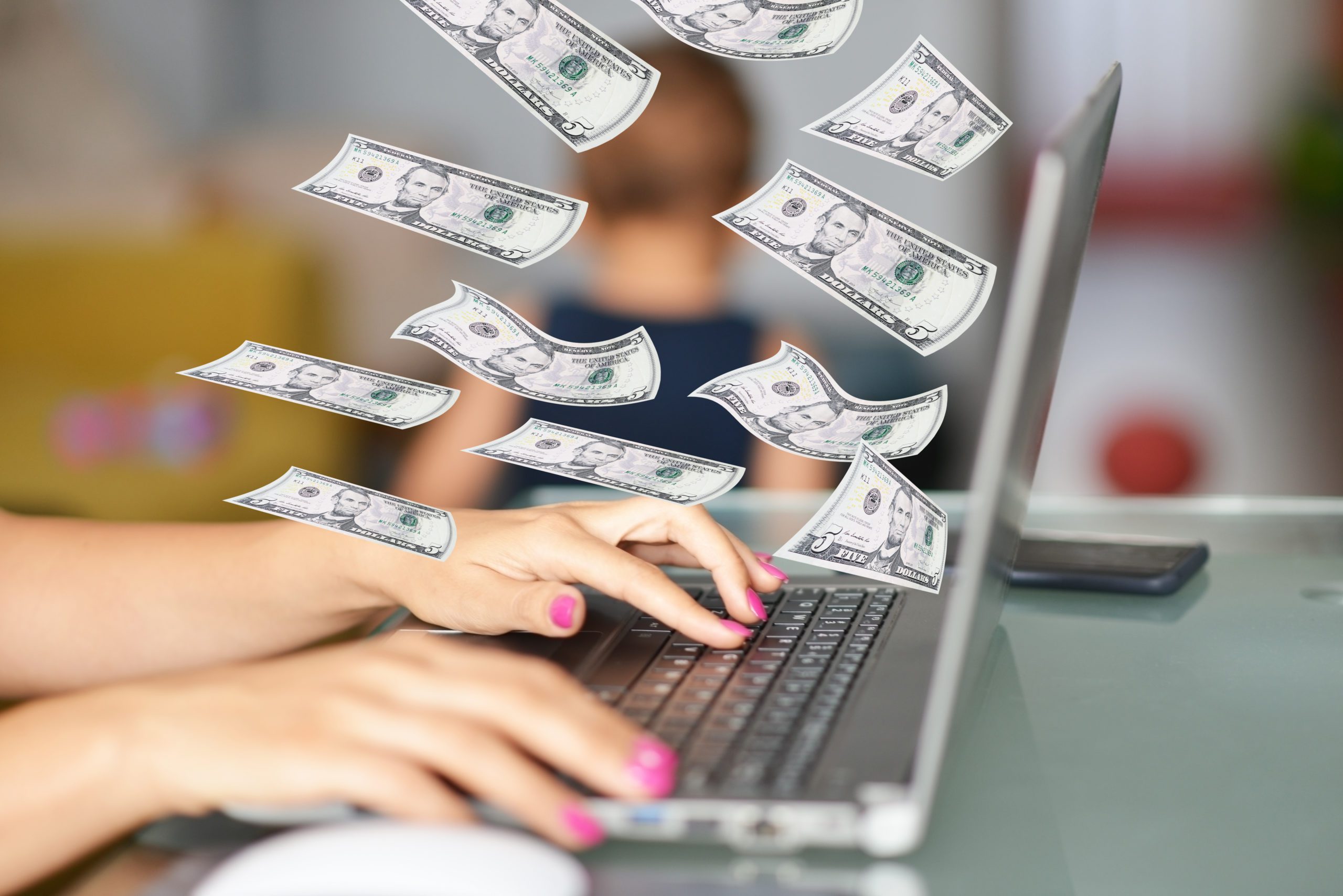 Work-from-home mom on her laptop with dollars flying around as her child plays in the background