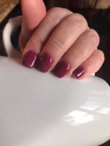 a woman's hand with burgundy dipped nails to illustrate dipping your nails at home