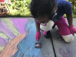 a child wearing knee pads and gloves smearing chalk onto a sidewalk