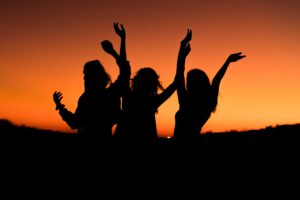 silhouette of women celebrating by throwing their hands up against the backdrop of the sunset