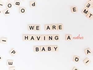 pregnancy announcement as scrabble letters spell out, "We are having another baby" on white background