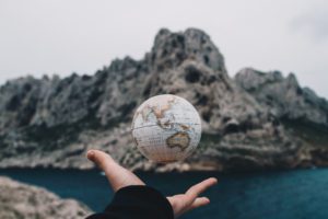 a hand tossing the globe with mountains in the background