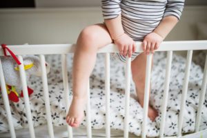 Toddler climbing out of his crib with one leg over the railing