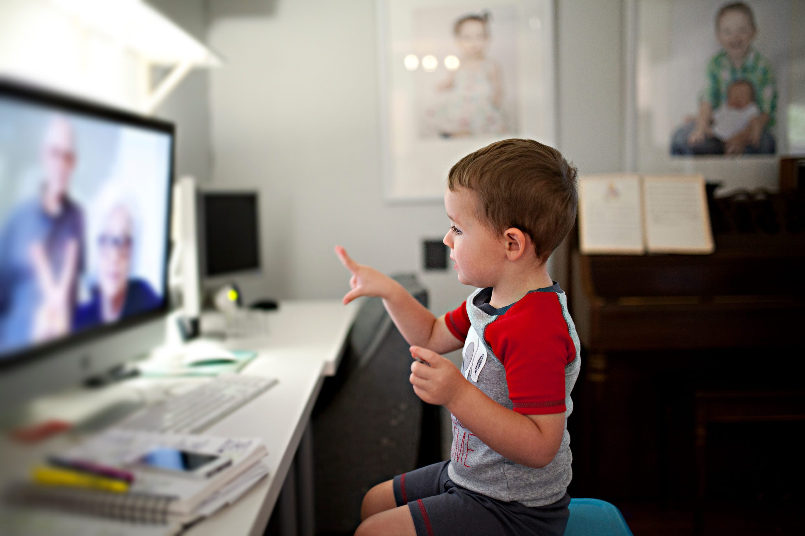 Young boy in a red and white shirt pointing to a computer screen on which his grandparents are featured