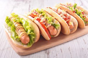 four hot dogs with lettuce, tomato, ketchup, and mustard on a wooden platter