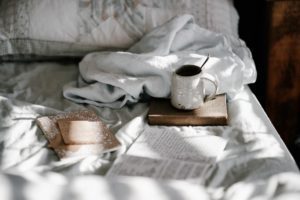 an unmade bed with books and a coffee mug to symbolize the comfort in confinement