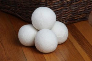 a close up of wool dryer balls stacked on a wooden floor by a wicker basket