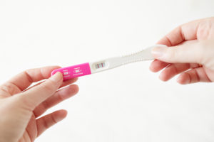 a woman's hands holding a positive pregnancy test against a white background