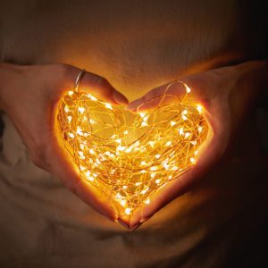 Close-up of lights in the shape of a heart, a woman holding in hands in the dark to symbolize a mother's heart lights the way