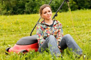 woman smirking as she sits next to a lawn mower