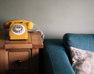 an image of a yellow phone on a wooden side table near a blue couch serving as a reminder to call your mom