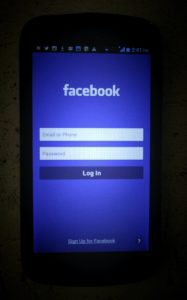 a phone screen lit up by the facebook blue background, on the login page