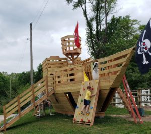 a wooden pirate ship playset complete with a climbing wall, slides, and pirate flags