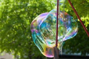 representing summer backyard activities, a close up of a giant bubble maker crafting a huge bubble against the backdrop of green leaves