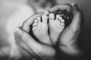 a black and white image of a mom holding a newborn baby's feet in her hands