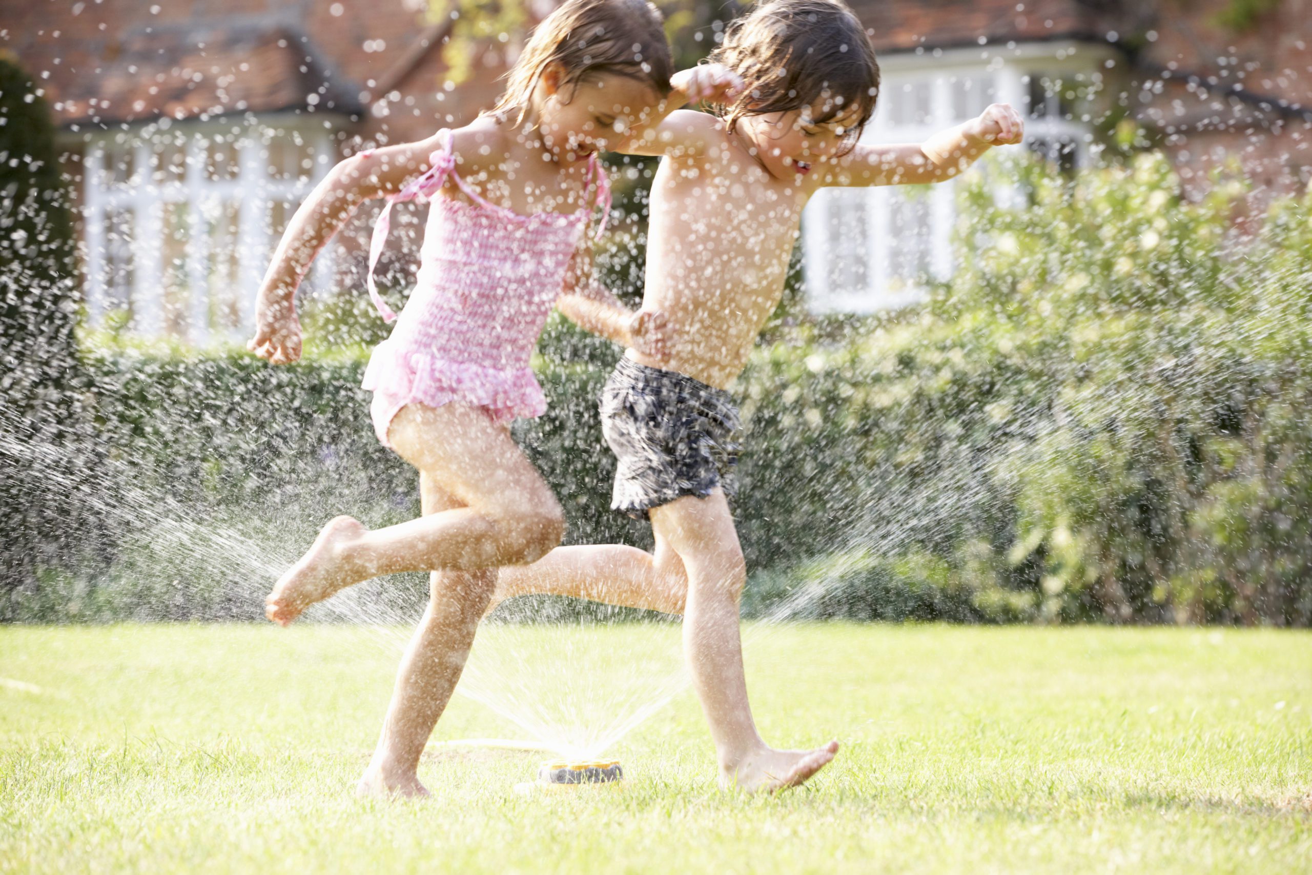 two children running through a garden sprinkler