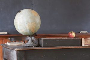 Vintage classroom showing blackboard behind apple and antique globe on teacher's desk