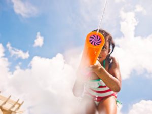 enjoying summer backyard activities, this little girl in a striped swimsuit squirts a water blaster
