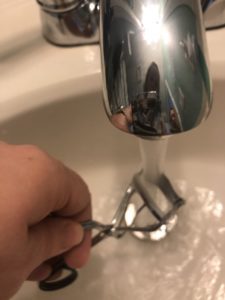 a photo of a woman running hot water on her eyelash curler as it makes it work better per one of the beauty tips she follows