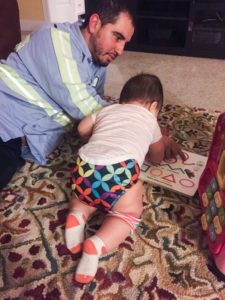 a dad sits sprawls on the floor with his baby as they read a book together