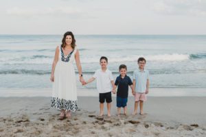 A mom standing on the shore with her three little boys
