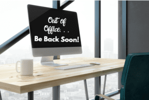 an office desk by a window with a computer screen that reads, "Out of Office, Be Back Soon" to represent maternity leave