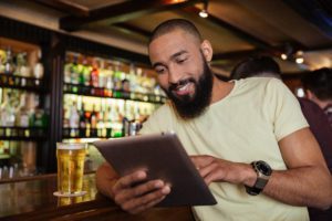 African american man drinking beer in pub and using tablet