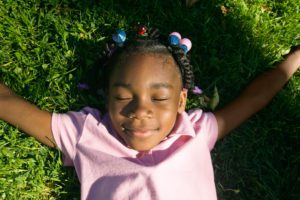 An African American girl, laying with her eyes closed and her arms outstretched in the grass