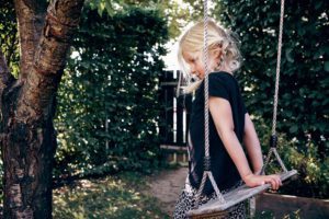 Shy little girl playing on a tree swing outdoors