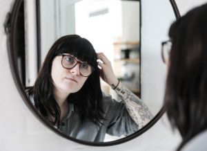 a mom with dark hair and glasses peering at herself in the mirror who needs to be reminded that she is enough
