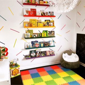 a colorful playroom with bookshelves, a multicolor playmat, and washi tape stripes on the walls