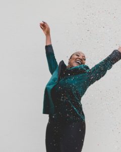 an African American woman with her arms up in the air as she tosses confetti