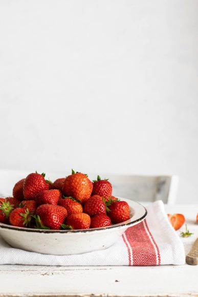 a white bowl filled with strawberries on a cloth dish towel on a white table to represent summer recipes you can make for dessert