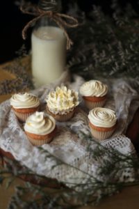 cupcakes with white icing on a cloth next to a white candle