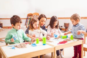children sitting on the floor with a mommy's helper playing with kinetic sand