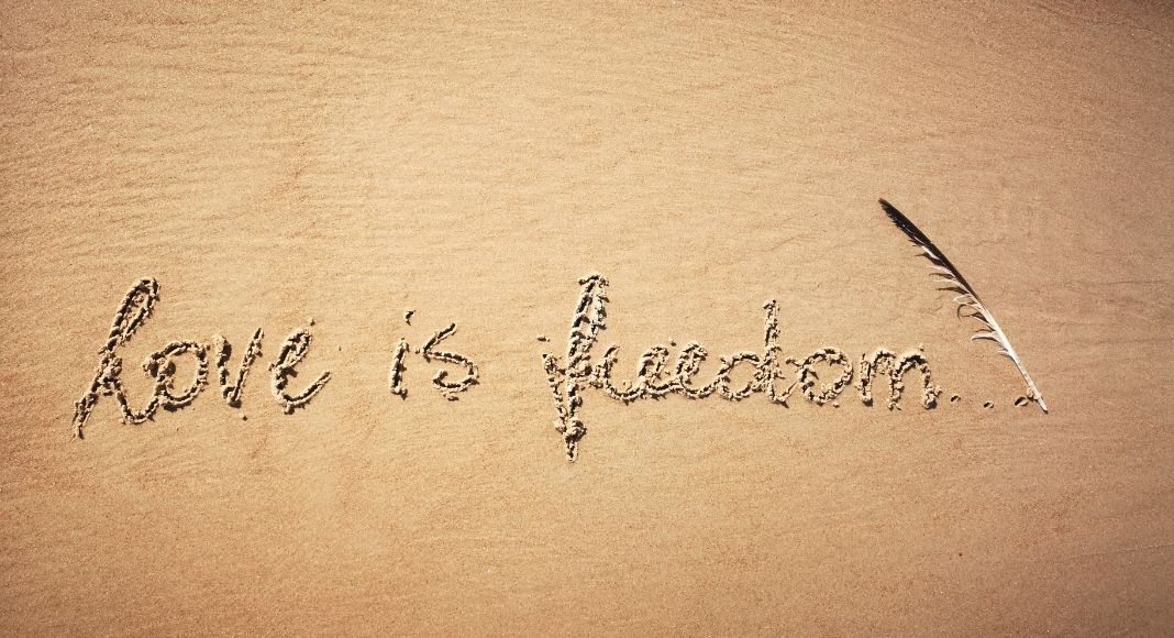 love is freedom written in the sand with a feather