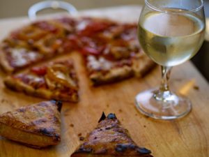 pizza on a cutting board with a glass of white wine