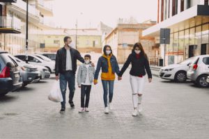a family walking in a parking lot, holding hands and wearing mask for COVID 19