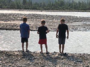 a photo from behind of three boys at a river's edge