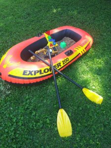 an inflatable boat filled with sand and toys in the backyard