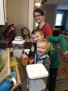 a mom with her three kids, and a counter strewn with baking supplies as she is cooking with kids