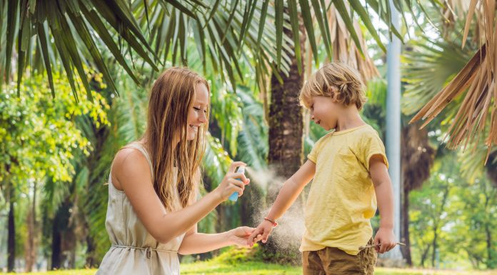 a mom and her son out in the grass as she sprays bug spray on him