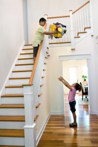 a boy at the top of the stairs tossing laundry down to his sister below